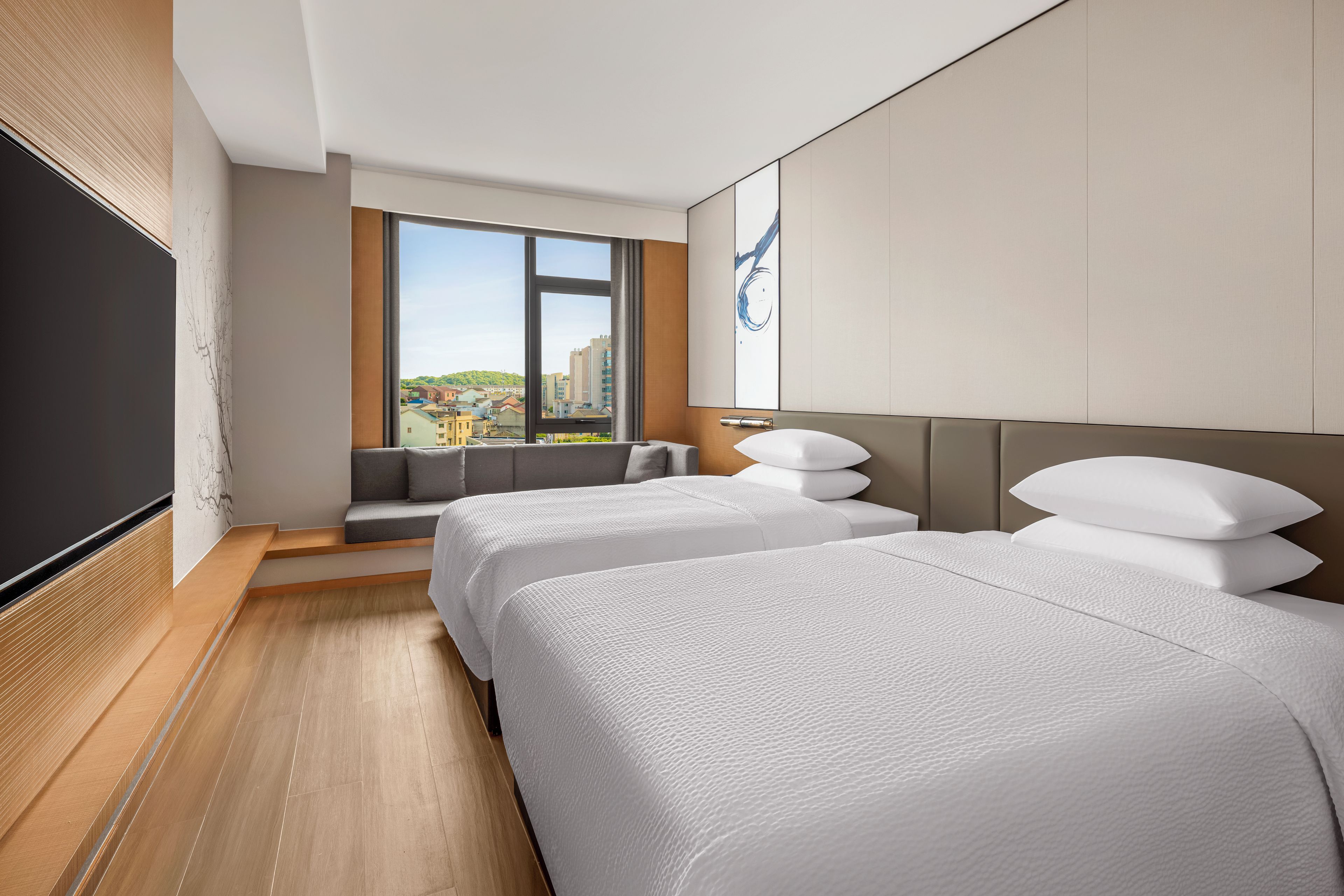 Habitación de hotel con dos camas, un ventanal grande y vistas a la ciudad.