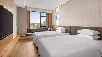 Habitación de hotel con dos camas, un ventanal grande y vistas a la ciudad.