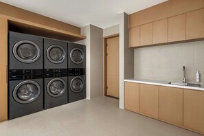 Un moderno lavadero con cuatro lavadoras Haier, armarios de madera y una encimera blanca con un grifo y una botella de Nivea.