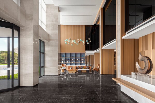 A modern hotel lobby with a marble floor, seating area, and a decorative wall with hanging lights.