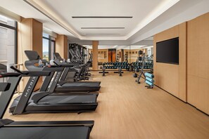 A modern gym with multiple treadmills, weight machines, and a mirror wall.