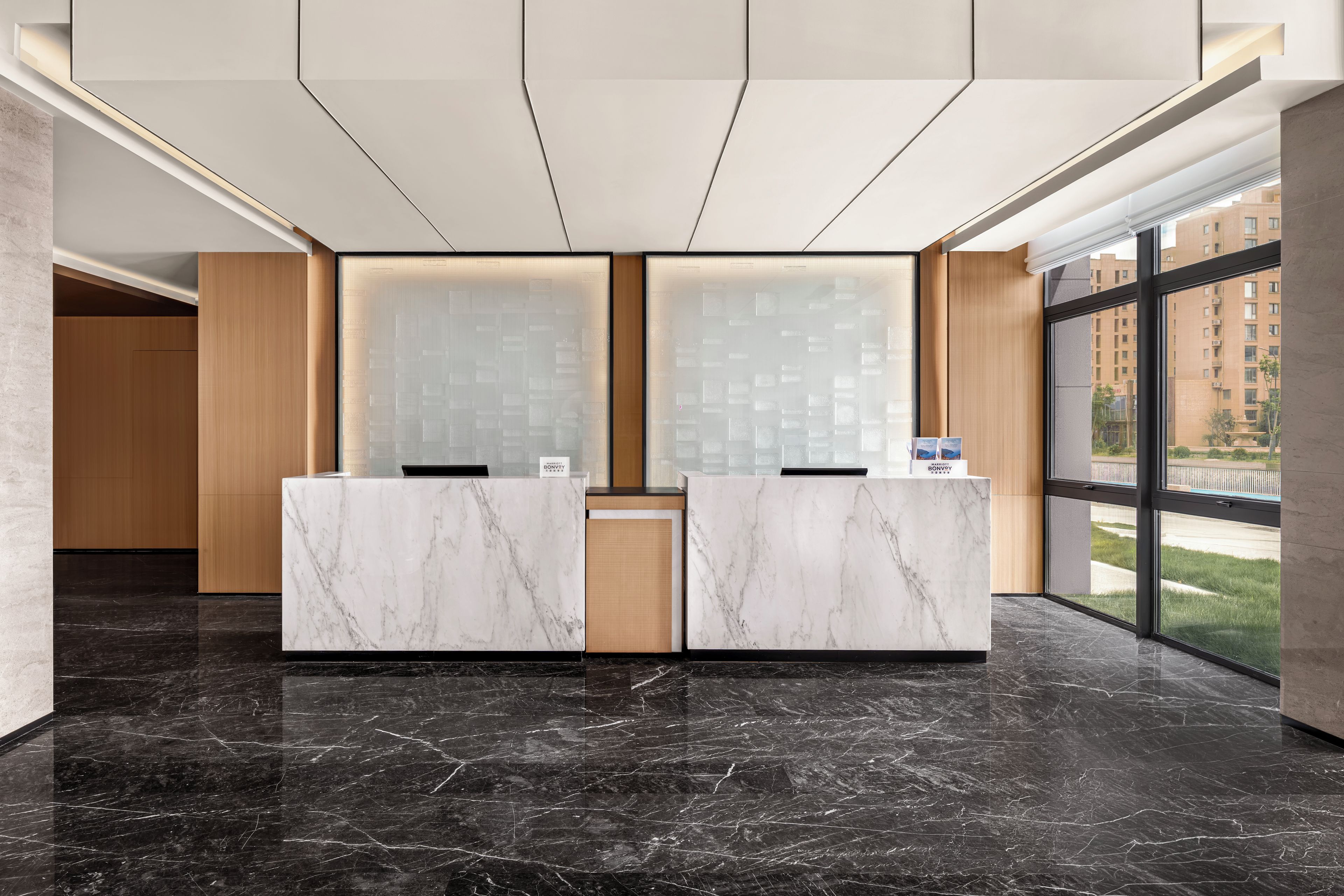 A reception desk with marble tops, a wooden panel wall, and a large window with a view of buildings.