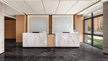 Un mostrador de recepción con encimeras de mármol, un panel de pared de madera y un amplio ventanal con vistas a edificios.