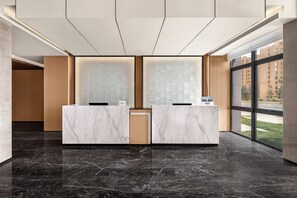 Un mostrador de recepción con encimeras de mármol, un panel de pared de madera y un amplio ventanal con vistas a edificios.