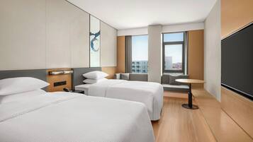 A hotel room with two beds, a small table, a sofa, and a large window offering a city view.