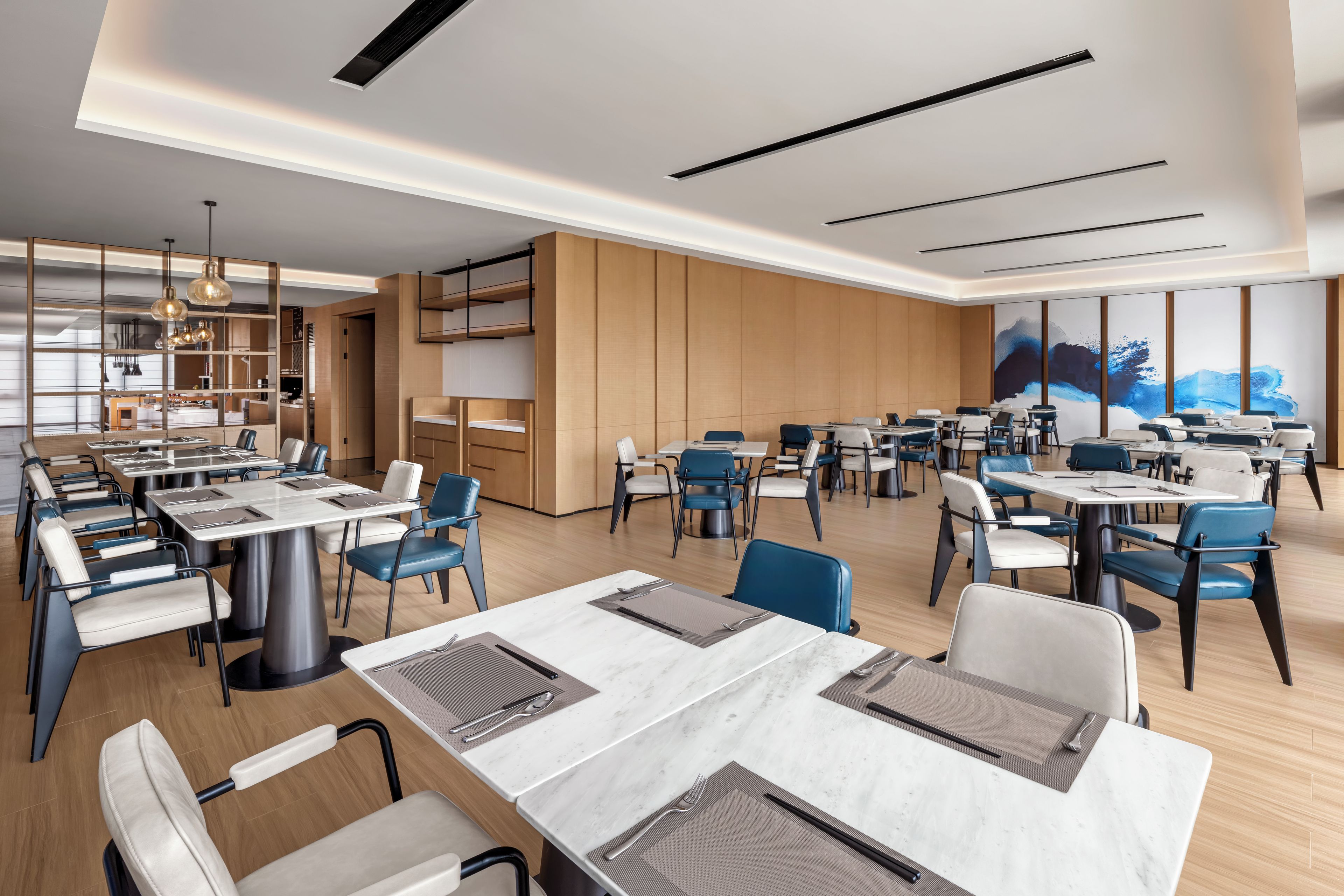 Een moderne eetruimte met meerdere tafels en stoelen, een keuken met kasten, en een groot raam met uitzicht.