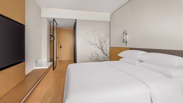A hotel room with a bed, a television, a wall-mounted light fixture, and a door leading to a hallway.