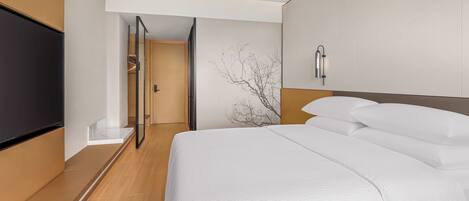 Een hotelkamer met een bed, een televisie, een wandlamp en een deur die naar een gang leidt.