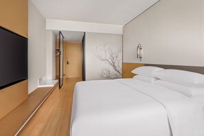 A hotel room with a bed, a television, a wall-mounted light fixture, and a door leading to a hallway.
