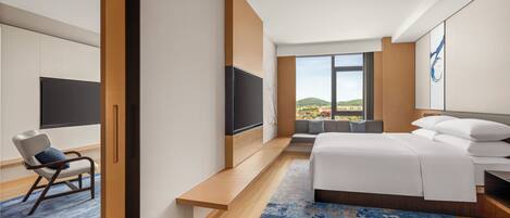 Ein modernes Hotelzimmer mit einem großen Bett, einem Flachbildfernseher, einer Sitzecke mit Blick und einem Holzboden.