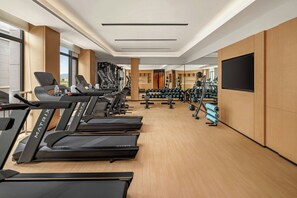 Un gimnasio con cintas de correr, máquinas de pesas y un espejo grande.