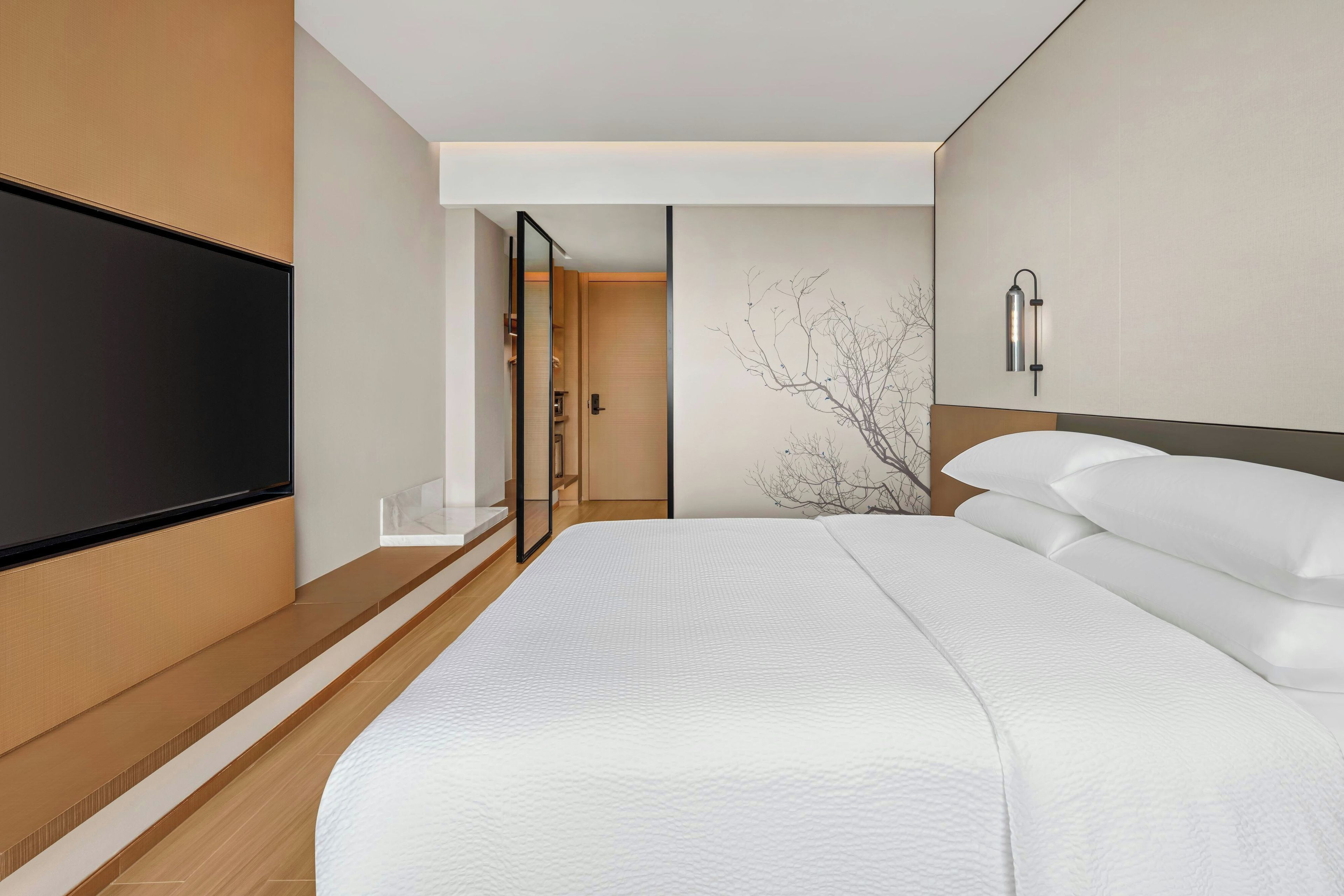 Een moderne hotelkamer met een groot bed, een flatscreen televisie aan de muur en een minimalistisch design.