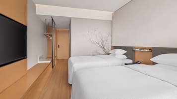 Een moderne hotelkamer met twee bedden, een flatscreen televisie, een nachtkastje met een lamp en een wandtelevisie.