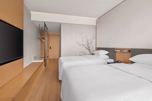 Una habitación de hotel moderna con dos camas, un televisor de pantalla plana, una mesita de noche con lámpara y un televisor montado en la pared.