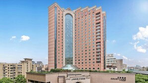 A high-rise hotel with a prominent central glass tower, a courtyard entrance, and a modern facade.