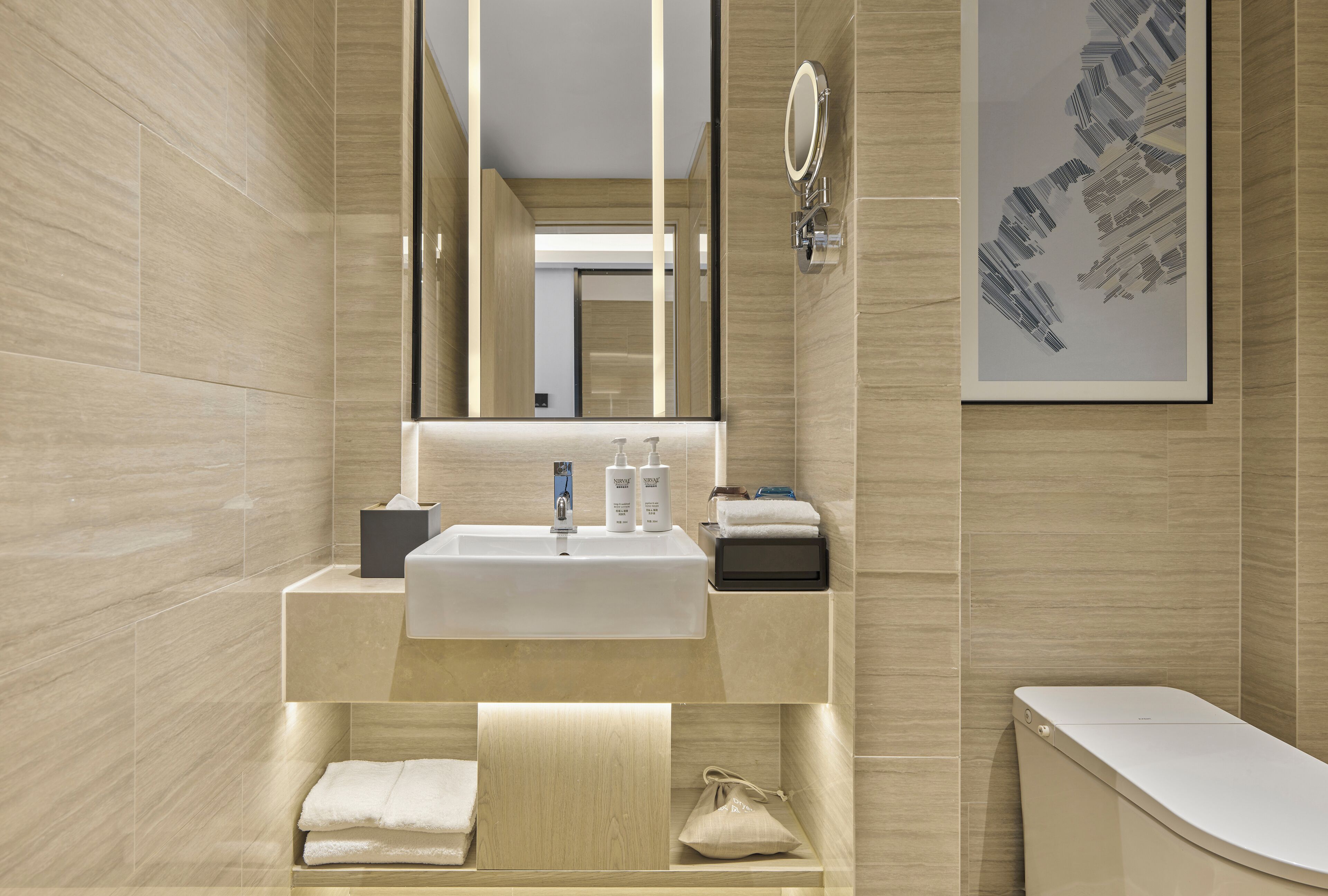 Une salle de bain moderne avec un grand miroir, un lavabo et des toilettes. On trouve des serviettes et des articles de toilette sur le comptoir.