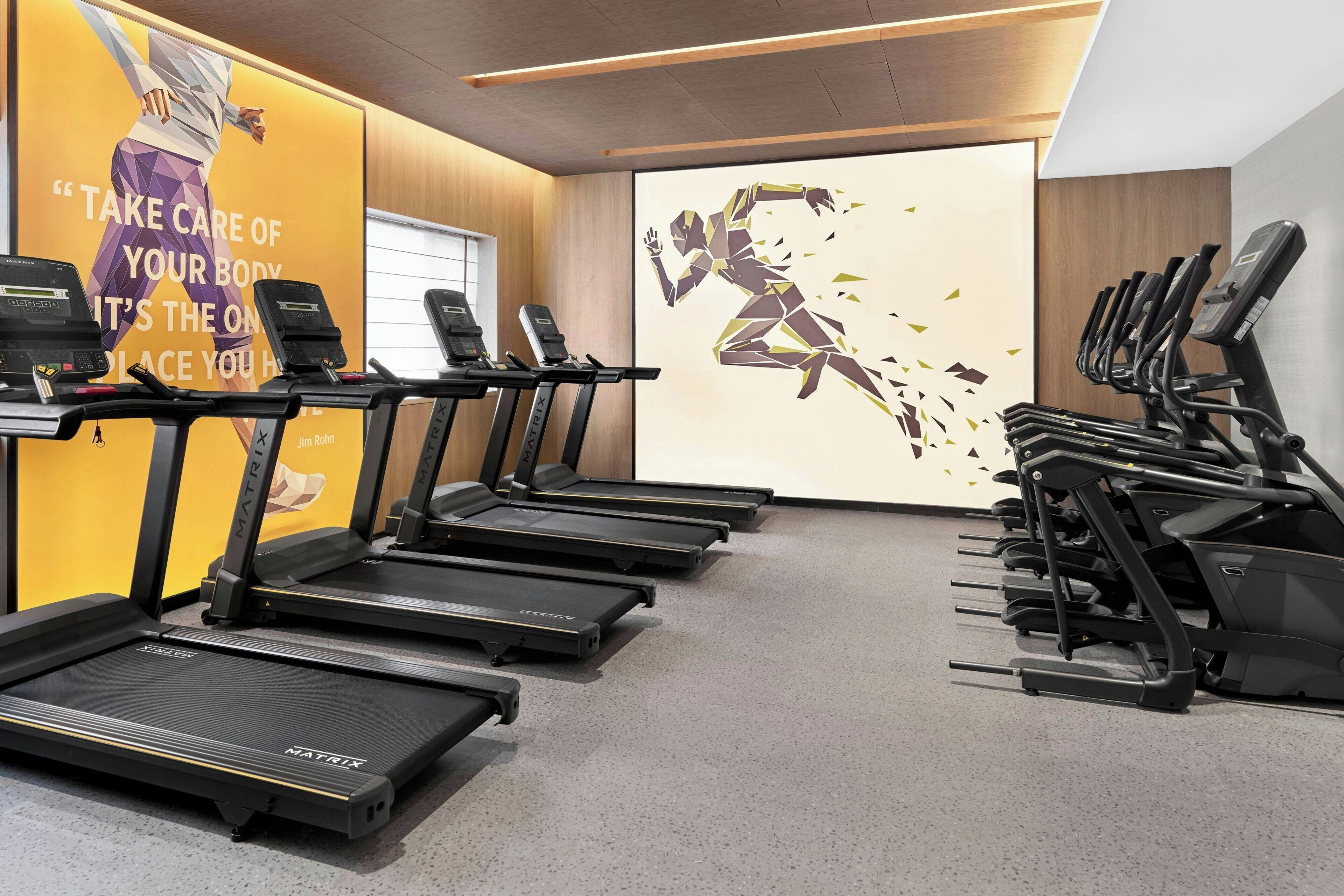 Un gimnasio con cintas de correr, un cartel motivacional y un ventanal grande.