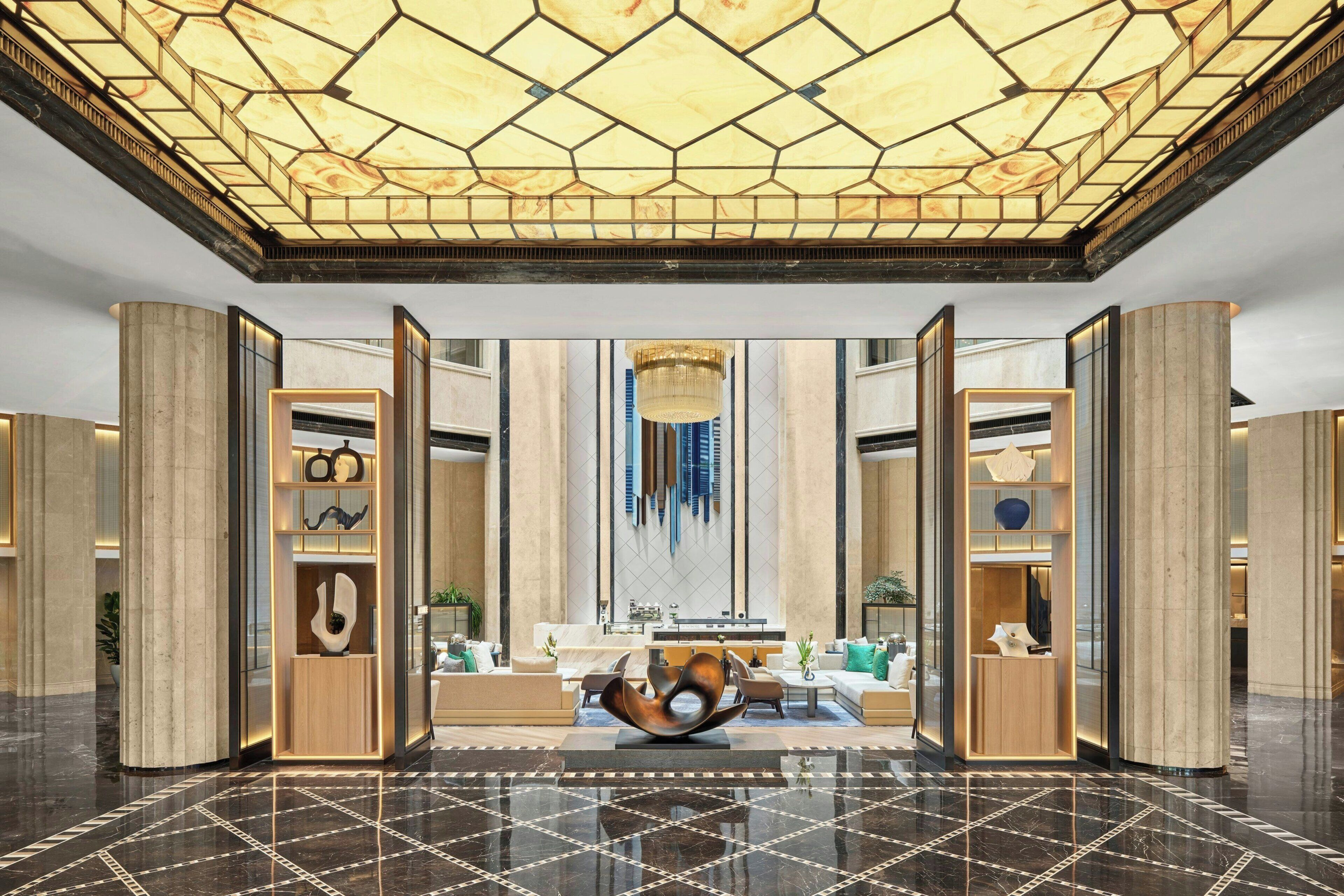 A spacious lobby with a geometric ceiling design, a central seating area, and modern furnishings.