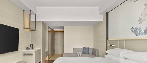 Una habitación de hotel moderna con una cama grande, un televisor de pantalla plana, una mesita de noche y una zona de estar con un sofá y una pequeña mesa.