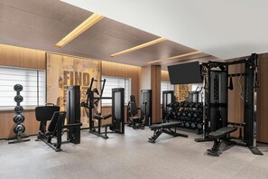 Un gimnasio con equipo de ejercicio variado, incluyendo mancuernas, una banca y máquinas de pesas.