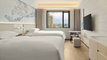 A hotel room with two beds, a small table, a TV, and a large window with a city view.