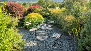 A garden patio with a table and chairs, surrounded by various plants and trees. - 2 Bed in Keswick (oc-sz082) (Threlkeld)