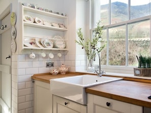 Una cocina con armarios blancos, encimera de madera, un lavabo blanco y una ventana con vistas a montañas.