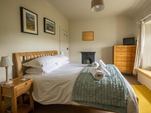 Una cama bien hecha con almohadas y una manta, una lámpara de noche, un aparador, un televisor y una chimenea.
