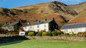 A row of white houses with solar panels, set against a mountainous backdrop. - 2 Bed in Keswick (oc-sz082) (Threlkeld)