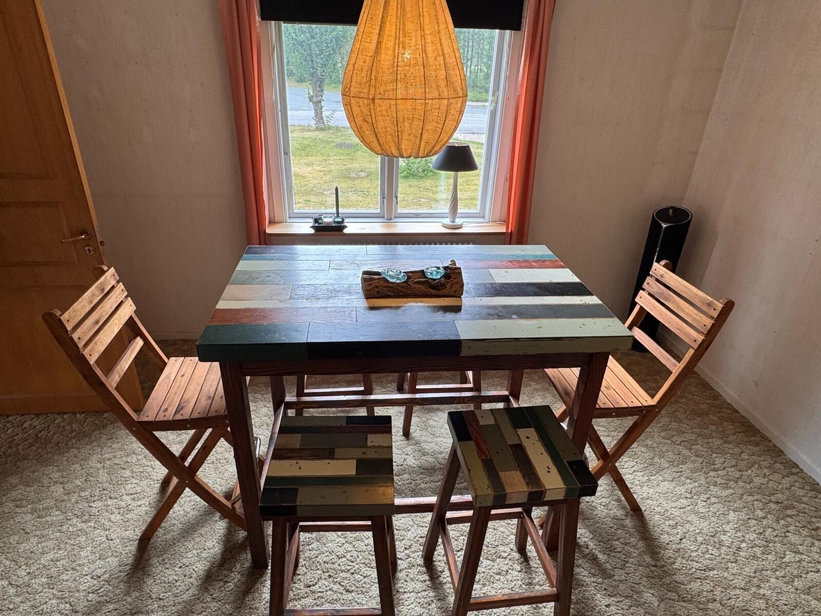 A dining table with a colorful tabletop and wooden chairs, positioned near a window with a view of the outdoors.
