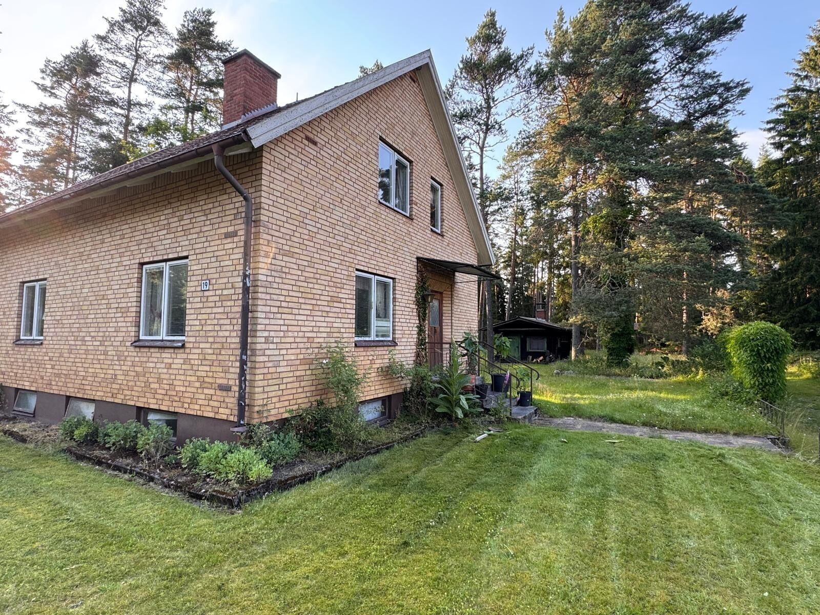 A two-story brick house with a sloped roof, a small porch, and a well-maintained garden.