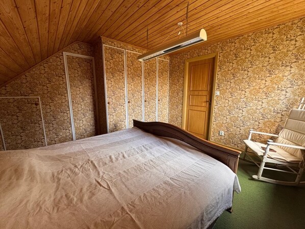 A bedroom with a bed, a rocking chair, a wardrobe, and a door.