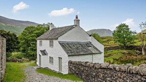 A white house with a stone wall, a gravel path, and green hills in the background. - 4 Bed in Buttermere (oc-sz090) (Buttermere)