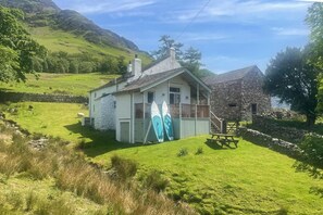A white house with a stone extension, a grassy yard, and two surfboards leaning against the house.