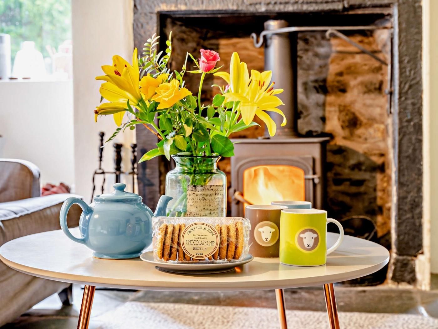 A table with a teapot, a glass jar of biscuits, a plate of biscuits, a vase with flowers, and a mug.