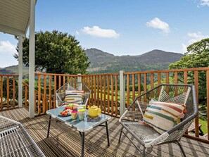 A balcony with wicker chairs, a table with food and a teapot, and a view of mountains.