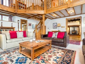 Ein geräumiger Wohnbereich mit einer Holztreppe, zwei Sofas mit roten Kissen, einem Couchtisch und einem gemusterten Teppich.