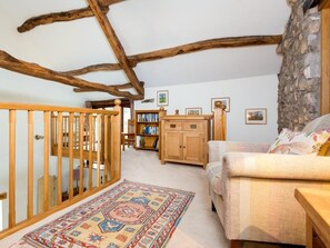Ein gemütliches Zimmer mit freiliegenden Holzbalken, einem Holckrippenbett, einer Couch, einem Bücherregal und einer Steinwand.