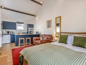 Habitación de hotel compacta con kitchenette, una cama con cubrecama a cuadros, un sofá de cuero y una alfombra roja pequeña.