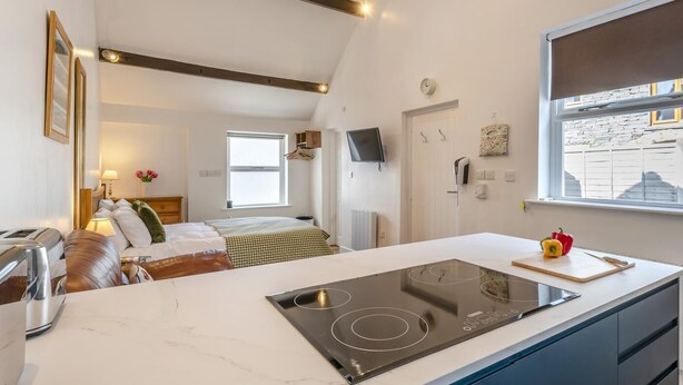 Et moderne køkken med indbygget komfur, et spiseområde med bord og stole, en seng med sengegavl og et vindue med udsigt til gaden.