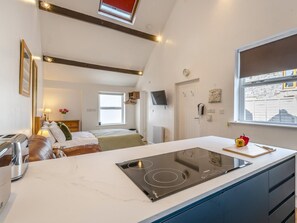 Une cuisine moderne dotée d’une cuisinière intégrée, un coin repas avec une table et des chaises, un lit avec une tête de lit et une fenêtre donnant sur la rue.