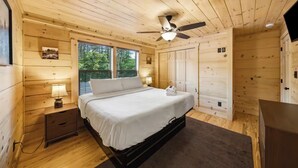 A wooden cabin bedroom with a bed, nightstand, lamp, ceiling fan, and windows. - New Build Cabin! Close to Mountains, Dollywood, Parkway, Pigeon Forge (Pigeon Forge)