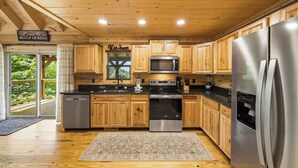 A modern kitchen with wooden cabinets, stainless steel appliances, and a sign reading 'Welcome to our NECK OF THE WOODS.' - New Build Cabin! Close to Mountains, Dollywood, Parkway, Pigeon Forge (Pigeon Forge)