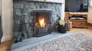 A stone fireplace with a fire, a television, and a wooden entertainment unit. - 2 Bed in Keswick (oc-sz068) (Borrowdale)