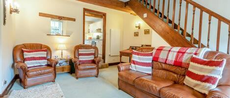 A living room with a staircase, leather armchairs, a sofa, and a rug.