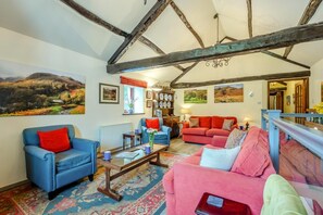 A cozy living room with a blue armchair, a pink sofa, and a red sofa. There are paintings on the walls, a bookshelf, and a window with curtains. - 3 Bed in Borrowdale (oc-sz465) (Borrowdale)