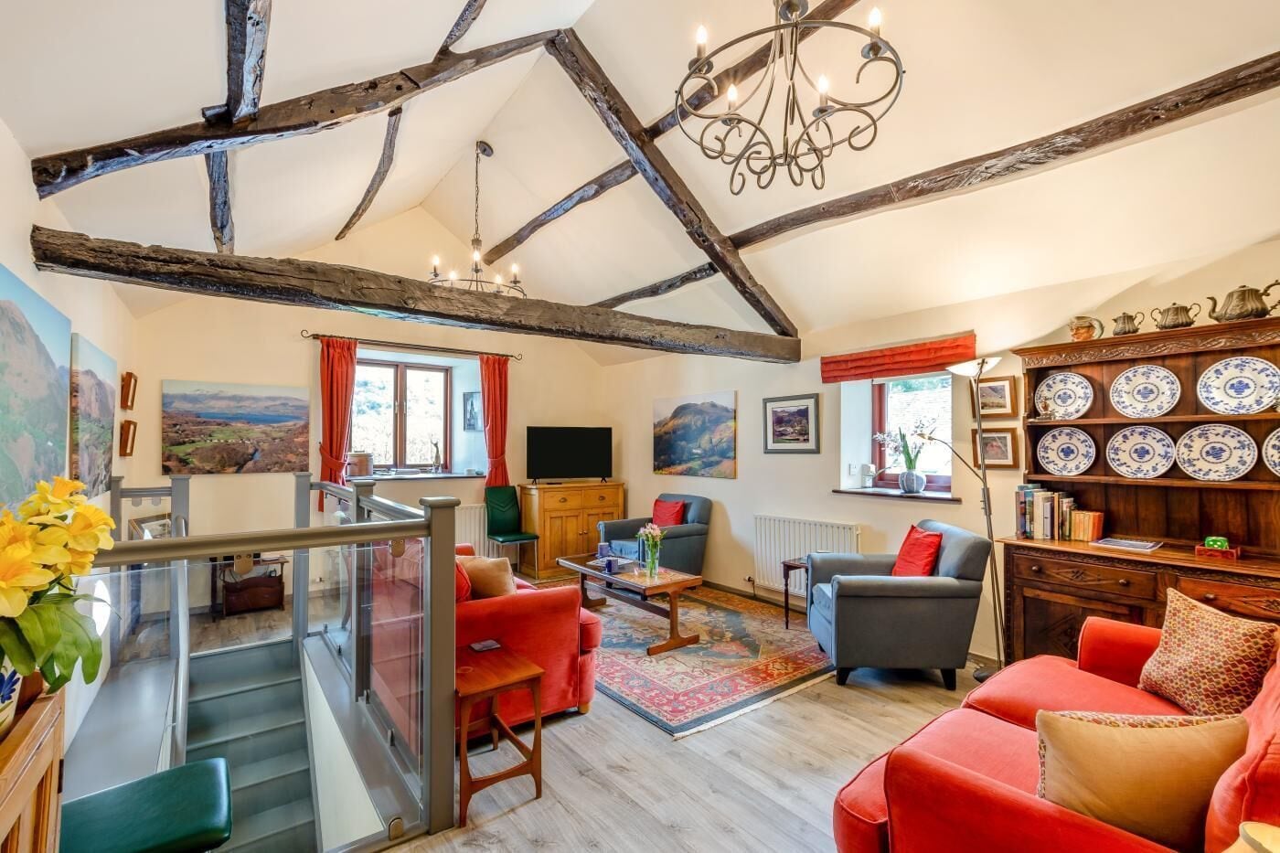A spacious living room with exposed wooden beams, a chandelier, a television, and a collection of decorative plates.