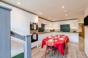 A modern kitchen with white cabinets, a built-in oven, and a dining area with a red tablecloth. - 3 Bed in Borrowdale (oc-sz465) (Borrowdale)