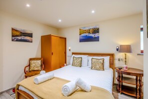 A hotel room with a bed, two chairs, a wooden wardrobe, a bedside table with a lamp, and two wall-mounted paintings. - 3 Bed in Borrowdale (oc-sz465) (Borrowdale)