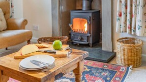A cozy living room with a fireplace, a dining table with plates and a knife, and a sofa. - 3 Bed in Cumbria (oc-sz101) (Crosthwaite and Lyth)